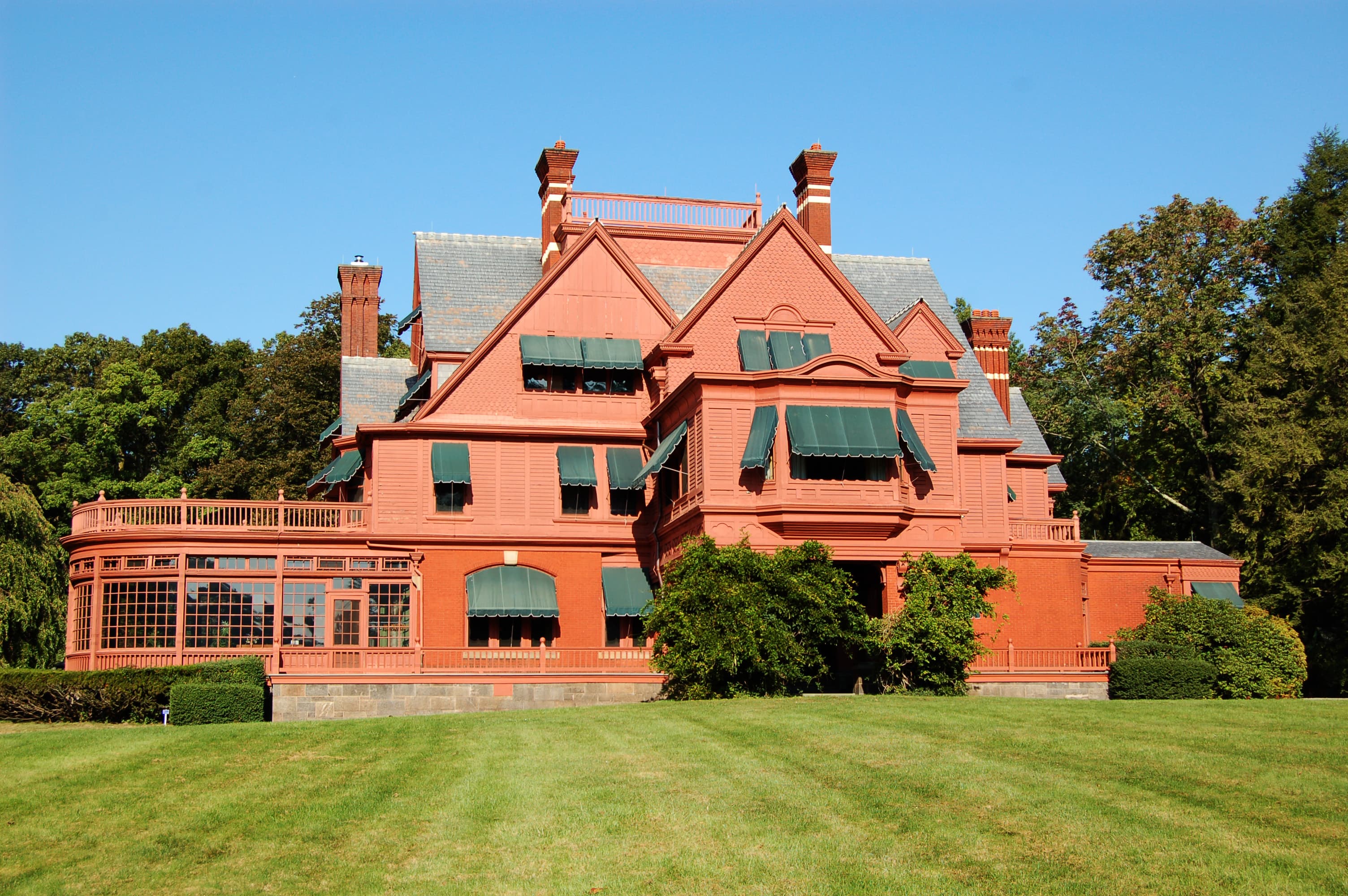 Large salmon colored Victorian mansion with green lawn and blue sky