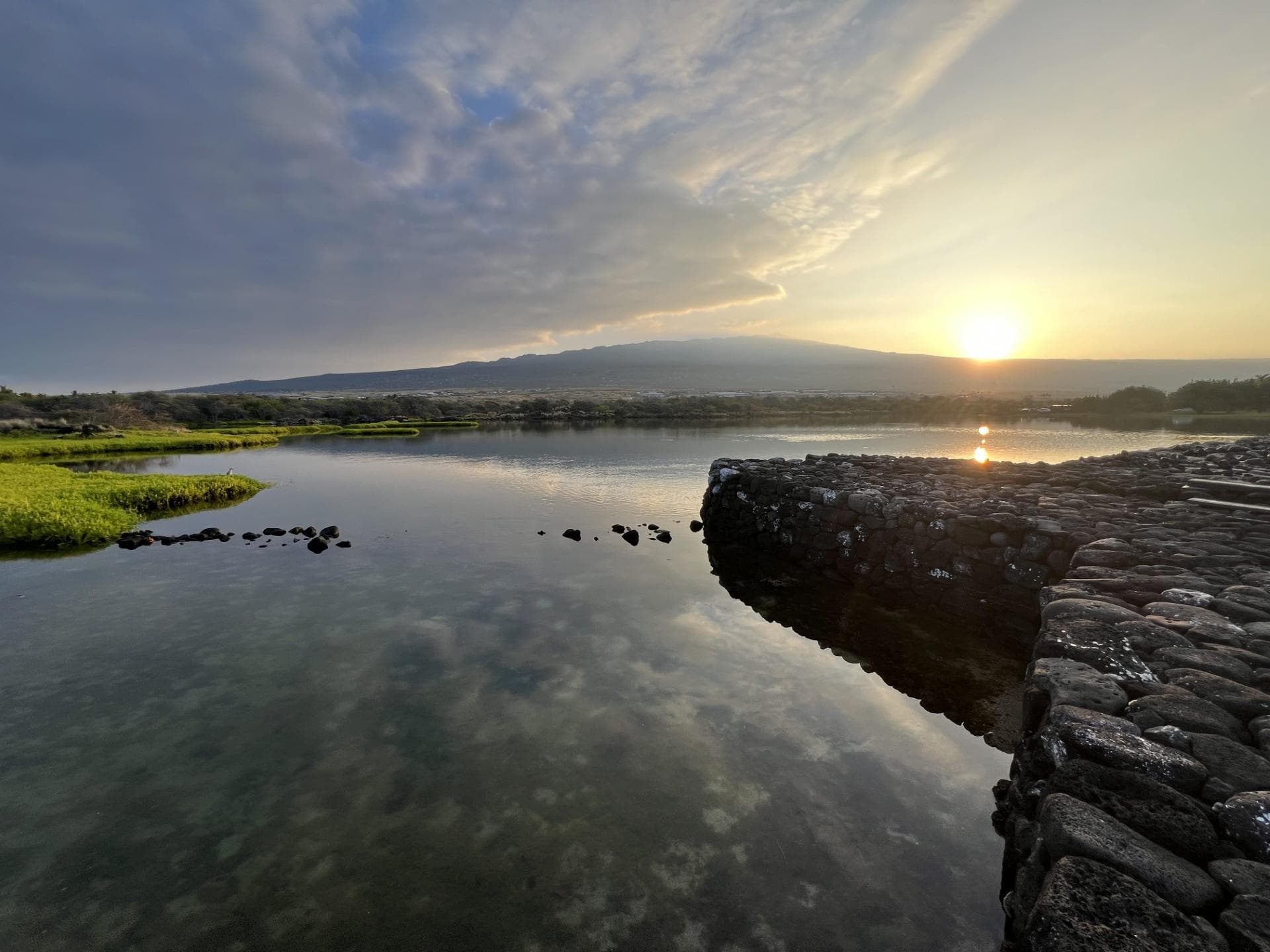 Sun rises over Hualālai volcano as seen from the Kaloko fishpond wall
